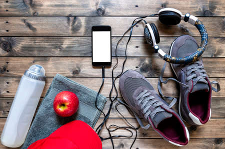 Top view of a red apple, sport shoes, audio headphone, smartphone, hat, towel and water bottle photographed on an antique wooden table. Text space.の写真素材