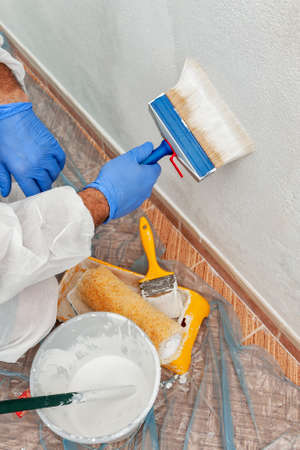 Close-up of the hand of a house painter at work painting a white wall with a paintbrushの写真素材