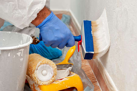 Close-up of the hand of a house painter at work painting a white wall with a paintbrushの写真素材