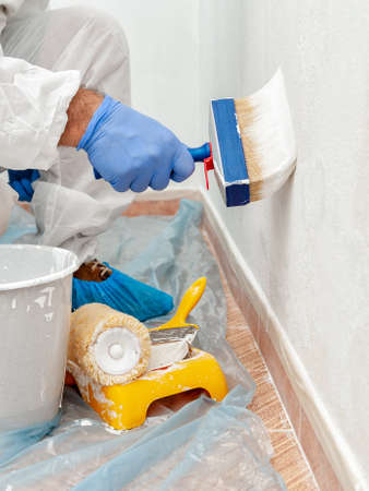 Close-up of the hand of a house painter at work painting a white wall with a paintbrushの写真素材