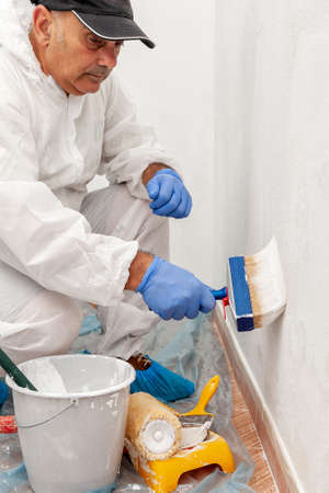 Workman house painter at work painting a white wall with a paintbrushの写真素材