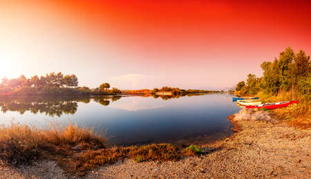 Beautiful landscape at sunrise of a pond with the reflection of the trees and the sky on the water. Old fishing boats on the shore. Petrosu pond, Orosei. Sardinia.の写真素材