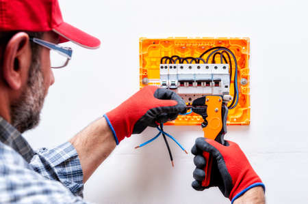 Electrician technician with glove-protected hands, works with the wire-cutter pliers in a...