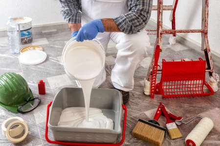 Caucasian house painter worker in white work overalls, pour the paint into the container. Construction industry.の写真素材