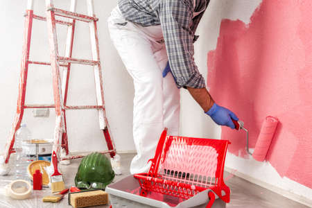 Caucasian house painter worker in white work overalls, with the roller painting the wall with colorful painting. Construction industry.の写真素材