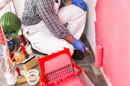 Caucasian house painter worker in white work overalls, with the roller he paints the wall with the colored painting of pink. Construction industry. Top view.の写真素材