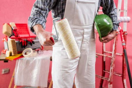 Caucasian house painter worker in white work overalls, with the roller to paint in hand. Construction industry. Work safety.の写真素材