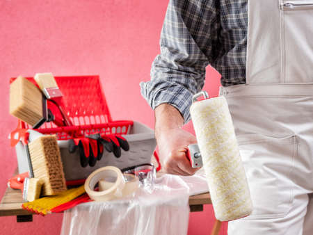 Caucasian house painter worker in white work overalls, with the roller to paint in hand. Construction industry. Work safety.の写真素材