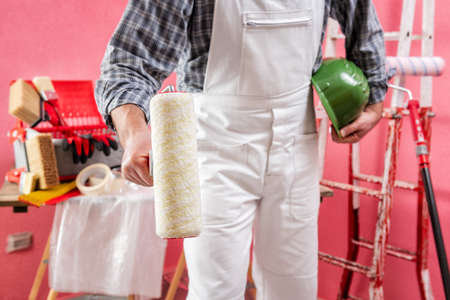 Caucasian house painter worker in white work overalls, with the roller to paint in hand. Construction industry. Work safety.の写真素材