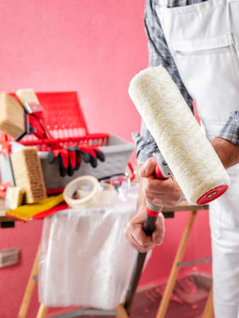 Caucasian house painter worker in white work overalls, he holds in his hands the roller with extension. Construction industry. Work safety.の写真素材