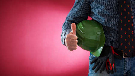 Caucasian architect engineer in jeans and shirt, with helmet and protective gloves making ok sign with thumb up. Construction industry. Work safety. Red background.の写真素材