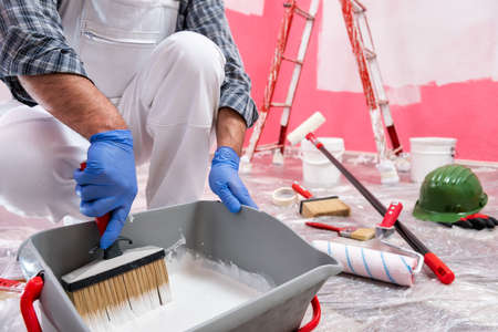 Caucasian house painter worker in white overalls, prepare the white paint to paint the pink wall. Construction industry. Work safety.の写真素材