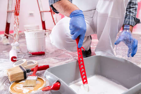 Caucasian house painter worker in white overalls, prepare the white paint to paint the pink wall. Construction industry. Work safety.の写真素材