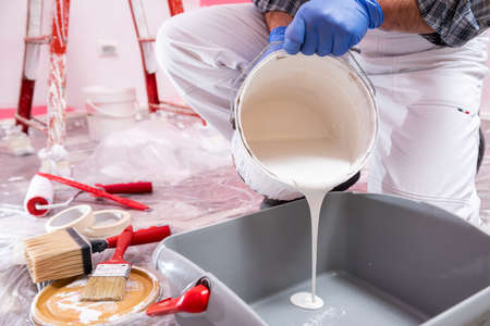 Caucasian house painter worker in white overalls, pour the white paint into the container. Construction industry. Work safety.の写真素材