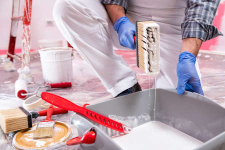 Caucasian house painter worker in white overalls, prepare the white paint to paint the pink wall. Construction industry. Work safety.の写真素材