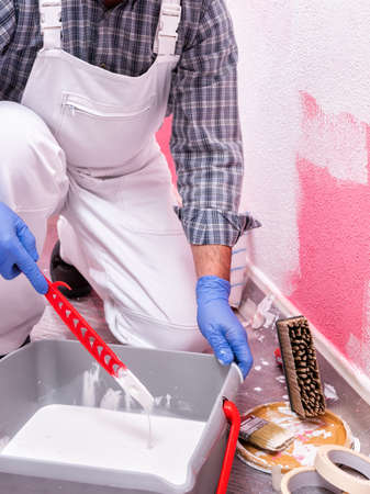 Caucasian house painter worker in white overalls, prepare the white paint to paint the pink wall. Construction industry. Work safety.の写真素材