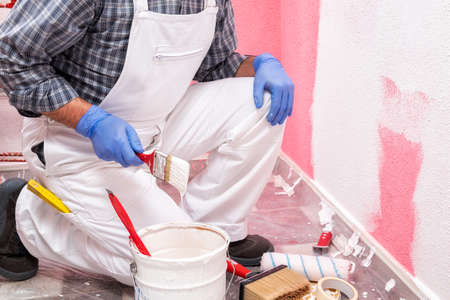 Caucasian house painter worker in white overalls, prepare the white paint to paint the pink wall. Construction industry. Work safety.の写真素材