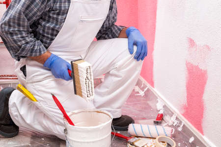 Caucasian house painter worker in white overalls, prepare the white paint to paint the pink wall. Construction industry. Work safety.の写真素材