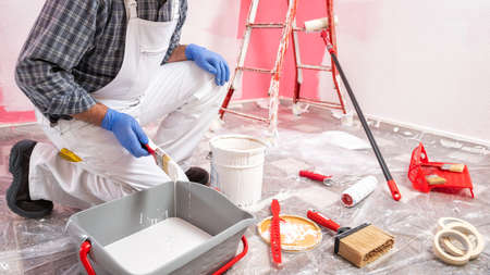 Caucasian house painter worker in white overalls, prepares the white paint to paint the pink wall. Construction industry. Work safety.の写真素材