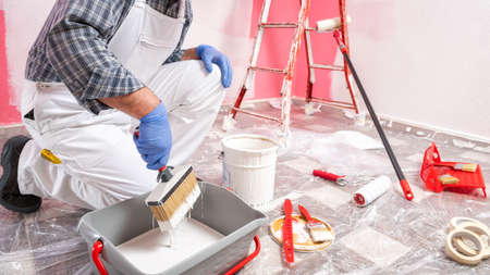 Caucasian house painter worker in white overalls, prepares the white paint to paint the pink wall. Construction industry. Work safety.の写真素材