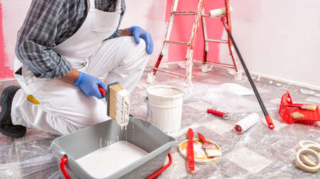 Caucasian house painter worker in white overalls, prepares the white paint to paint the pink wall. Construction industry. Work safety.の写真素材