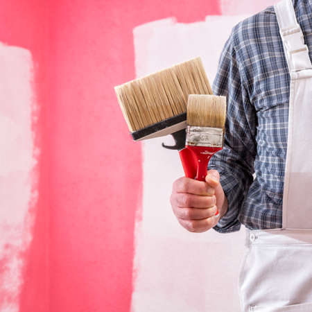Caucasian house painter worker in white overalls, he holds the brush for painting in hand. Construction industry. Work tools.の写真素材