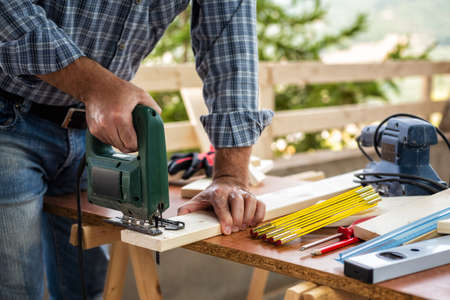Adult craftsman carpenter with electric saw working on cutting a wooden table. Housework do it yourself. Stock photography.の写真素材