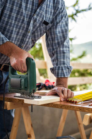 Adult craftsman carpenter with electric saw working on cutting a wooden table. Housework do it yourself. Stock photography.の写真素材