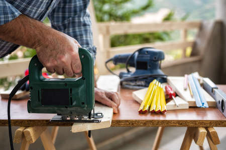 Adult craftsman carpenter with electric saw working on cutting a wooden table. Housework do it yourself. Stock photography.の写真素材