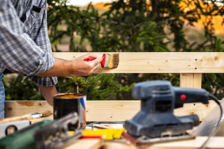 Adult craftsman carpenter with the brush painting the boards of a wooden fence. Housework do it yourself. Stock Photography.の写真素材