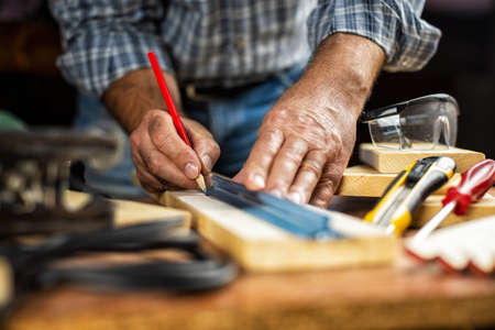 Adult craftsman carpenter with pencil and ruler tracing the cutting line on a wooden table. Housework do it yourself. Stock photography.の写真素材
