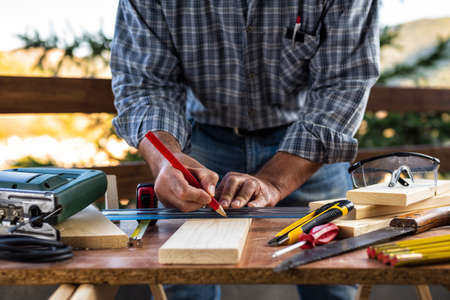 Adult craftsman carpenter with pencil and ruler tracing the cutting line on a wooden table. Housework do it yourself. Stock photography.の写真素材