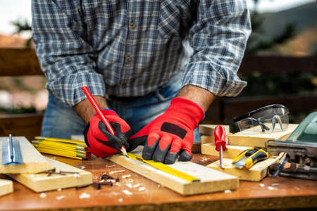 Craftsman adult carpenter with his hands protected by work gloves, measuring a wooden table. Housework do it yourself. Stock photographyの写真素材
