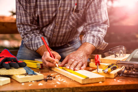Adult craftsman carpenter with the meter measuring a wooden table. Housework do it yourself. Stock photography. Glow sunset.の写真素材