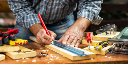 Adult craftsman carpenter with pencil and ruler tracing the cutting line on a wooden table. Housework do it yourself. Stock photography.の写真素材