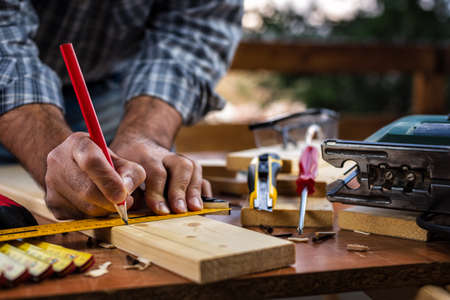 Adult carpenter craftsman with a pencil and the carpenter's square trace the cutting line on a wooden table. Construction industry, housework do it yourself. Stock photography.の写真素材