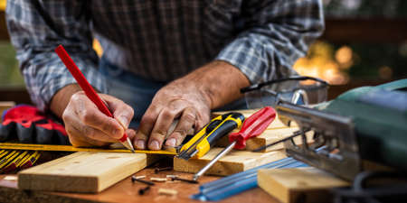 Adult carpenter craftsman with a pencil and the carpenter's square trace the cutting line on a wooden table. Construction industry, housework do it yourself. Stock photography.の写真素材