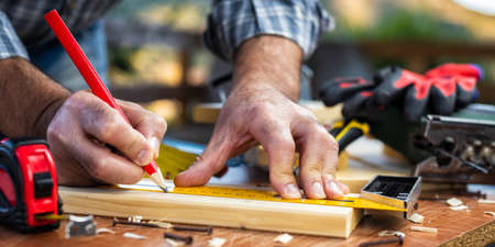 Adult carpenter craftsman with a pencil and the carpenter's square trace the cutting line on a wooden table. Construction industry, housework do it yourself. Stock photography.の写真素材