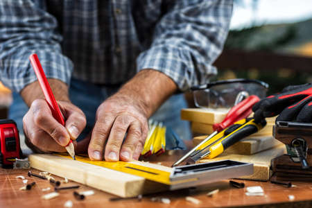 Adult carpenter craftsman with a pencil and the carpenter's square trace the cutting line on a wooden table. Construction industry, housework do it yourself. Stock photography.の写真素材