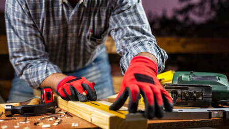 Adult carpenter craftsman wears protective gloves, with a pencil and the carpenter's square trace the cutting line on a wooden table. Construction industry, housework do it yourself. Stock photography.の写真素材