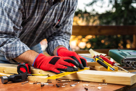 Adult carpenter craftsman wears protective gloves, with a pencil and the carpenter's square trace the cutting line on a wooden table. Construction industry, housework do it yourself. Stock photography.の写真素材