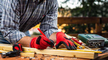 Adult carpenter craftsman wears protective gloves, with a pencil and the carpenter's square trace the cutting line on a wooden table. Construction industry, housework do it yourself. Stock photography.の写真素材