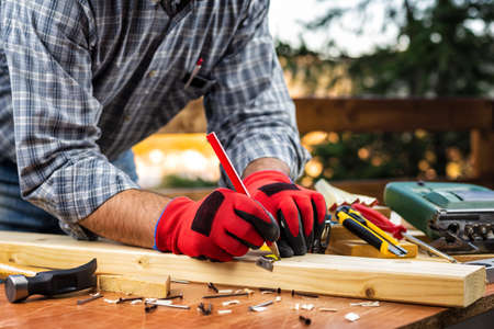 Adult carpenter craftsman wears protective gloves, with the meter takes the measure on a wooden table. Construction industry, housework do it yourself. Stock photography.の写真素材