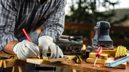 Adult carpenter craftsman wears protective leather gloves, with a pencil and the carpenter's square trace the cutting line on a wooden table. Construction industry, housework do it yourself. Stock photography.の写真素材
