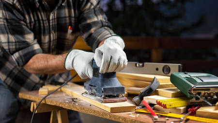 Adult carpenter craftsman wears protective leather gloves, with the electric sander smoothes a wooden table. Construction industry, housework do it yourself. Safety at work.の写真素材