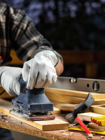 Adult carpenter craftsman wears protective leather gloves, with the electric sander smoothes a wooden table. Construction industry, housework do it yourself. Safety at work.の写真素材
