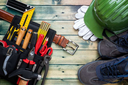 View from above of the bag with carpenter's work tools on an antique wooden table. Helmet, work shoes, leather gloves and protective goggles. Industry construction and do it yourself housework. Stock photography.の写真素材