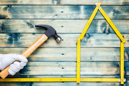 Top view of a hand protected by leather work gloves that holds the carpenterâs hammer on an antique wooden table. House concept made with the meter. Industry construction and do it yourself housework. Stock photography.の写真素材