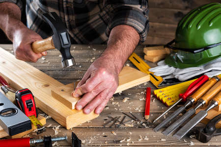 Close-up. Carpenter with hammer and nails fixes a wooden board. Construction industry, do it yourself. Wooden work table.の写真素材