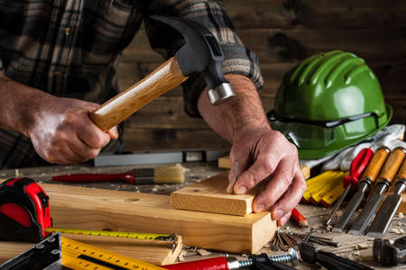 Close-up. Carpenter with hammer and nails fixes a wooden board. Construction industry, do it yourself. Wooden work table.の写真素材